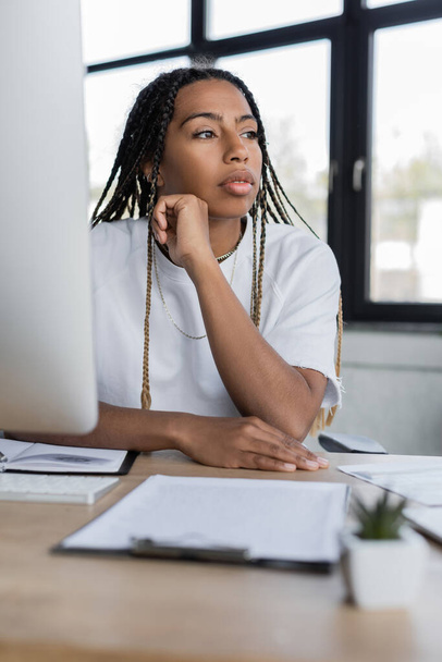 African american businesswoman looking away near computer and clipboard in office  - Foto, Bild