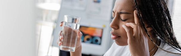 Africký americký manažer trpící bolestí hlavy a držící sklenici vody v kanceláři, prapor  - Fotografie, Obrázek