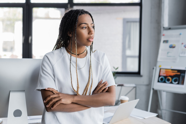 African american businesswoman in t-shirt looking away near devices on table in office  - Photo, image