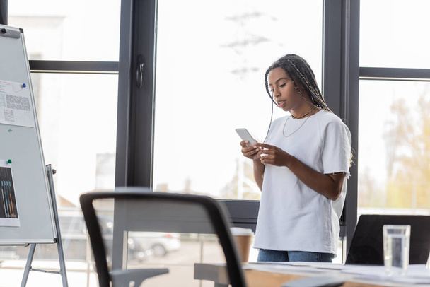 Afro-Amerikaanse zakenvrouw in casual kleding met behulp van smartphone in het kantoor  - Foto, afbeelding