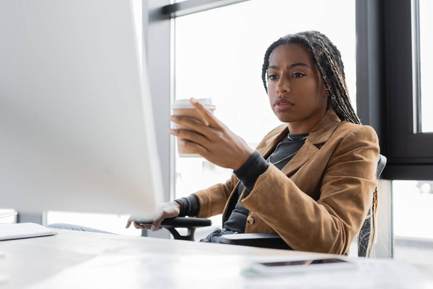 African american businesswoman holding coffee to go near computer in office  - Photo, Image