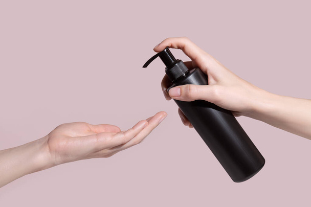 Uma mão de mulher com uma garrafa de plástico preto com uma bomba. Mockup. Foto de alta qualidade - Foto, Imagem