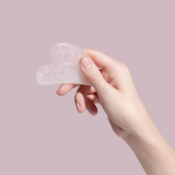 A female hand holding gua sha face massager on pink background. High quality photo - Foto, immagini