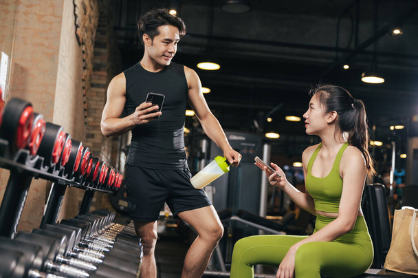 Азіатський чоловік і жінка в спортивній манері за допомогою смартфона і спілкуються в спокої після вправ у фітнес-залі. Спортивні люди ведуть активний спосіб життя.. - Фото, зображення