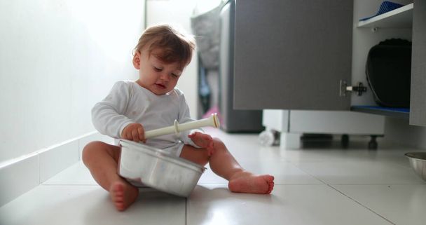 Baby boy hitting metal kitchen utensil on floor. One year old toddler drumming pans and pots - Foto, Bild
