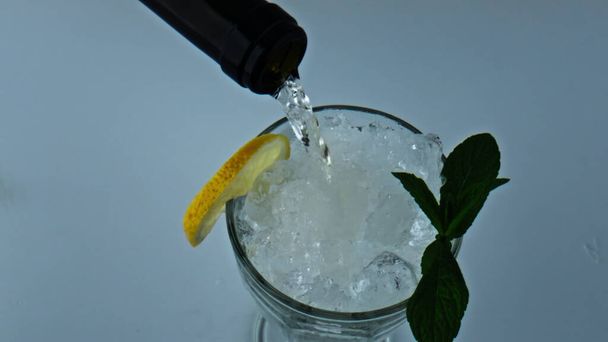 Пляшка наливає рідкий коктейль крупним планом. Освіжаючий крижаний лимонний м'ятний напій. Прохолодне вино, що наповнює чашку цитрусового алкоголю. Виготовлення смачного лимонаду мохіто для вечірки на вихідних. концепція літньої релаксації
. - Фото, зображення
