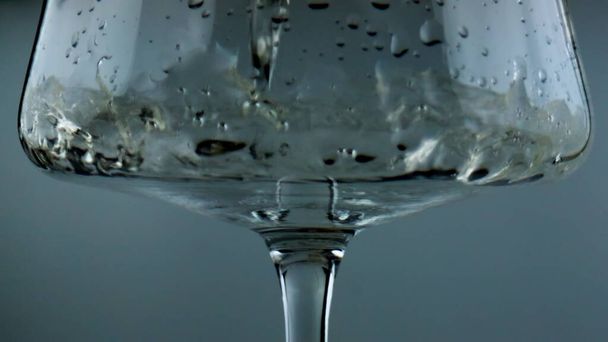 White wine filling glass closeup. Sparkling golden alcohol pouring splashing in goblet. Beautiful shot of air bubbles flowing tasty sauvignon in transparent cup. Romantic evening preparation concept - Foto, Imagen