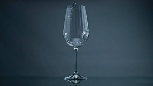 Water pouring wine glass at dark background closeup. Clear liquid splashing in beautiful transparent jug. Mineral fluid fill flowing into glassware. Refreshing drink beverage healthy lifestyle concept - Foto, afbeelding