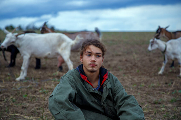 A teenage boy grazes goats in a field. A shepherd with goats in a field against a stormy sky. The concept of animal husbandry, survival, household.  - Foto, imagen