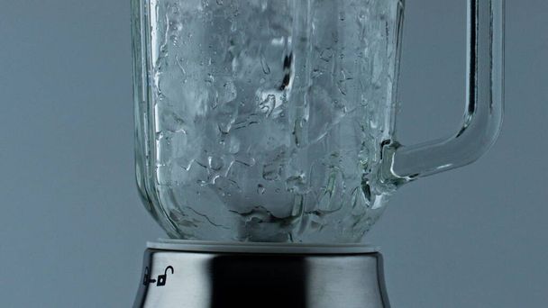Blender crushing ice pieces closeup. Cocktail mixer grinding cubes for beverage. Barkeeper machine preparing refreshing cool drink for summer party celebration. Mixing iced frozen chunks in container. - 写真・画像