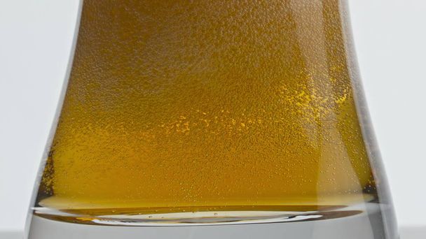 Lesní ledové pivo syčící na skleněné dno. Chmelová alkoholická tekutina v průhledném poháru zpomaluje. Pasterizované ječmen ležák bublající plavidlo bílé pozadí. Opojný nápoj - Fotografie, Obrázek