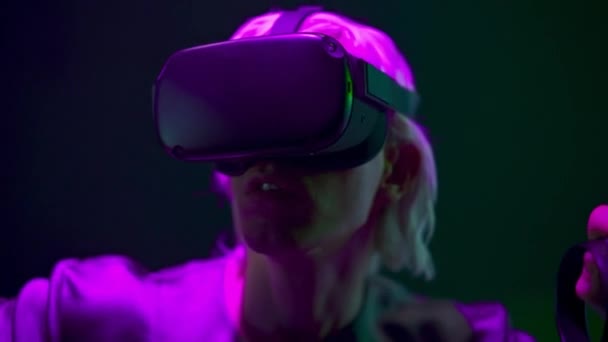 Amazed man playing videogame with remote controllers closeup. Focused gamer using joysticks and VR goggles at neon light place. Blonde headset guy interacting digital interface alone. Future concept  - Video, Çekim