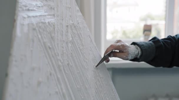 Неузнаваемая женщина создатель женских рук художник дизайнер неизвестная девушка держа шпаклевый нож гладкий фон делает фон с лопаточным оборудованием распространяется липкий белый клей текстуры на холсте - Кадры, видео