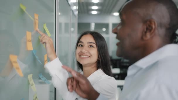 Corporate team business partners colleagues look at paper memo stickers on wall discuss project giving business advice managing tasks structure sticky notes brainstorming teamwork at office meeting - Footage, Video