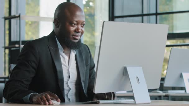 Afro-Amerikaanse zakenman commerciële agent expert site in modern kantoorwerk op de computer ontwikkelen website codering programma zoekgegevens online e-commerce marketing e-mailen draait hoofd op camera glimlachen - Video