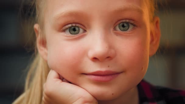Közelkép portré kis aranyos lány angyali szőke lány nagy zöld szemekkel gyönyörű kaukázusi gyerek óvodás imádnivaló kis modell nézi kamera otthon ül boldog gyermekkor fiatal generáció - Felvétel, videó