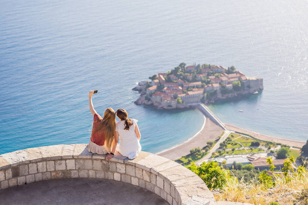 Two Woman tourist on background of beautiful view of the island of St. Stephen, Sveti Stefan on the Budva Riviera, Budva, Montenegro. Travel to Montenegro concept. - Foto, imagen