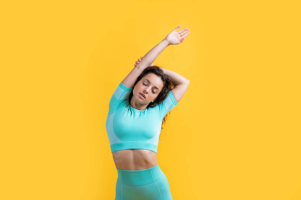 Athletic woman doing side stretch studio. Active woman isolated on yellow. Workout for flexibility and fitness. Relaxing stretching workout. - Foto, Imagem