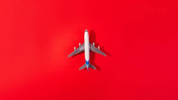 Bovenaanzicht van wit modelvliegtuig, vliegtuigspeelgoed op geïsoleerde rode achtergrond. Vlak lag met kopieerruimte. Reisbanner of reisbanner - Foto, afbeelding