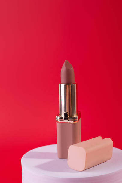 Nude, beige Lipstick on White Podium on red background. Design Template of Fashion Cosmetics Product for Ads, flyer, banner or Magazine Background.  - Foto, Imagem