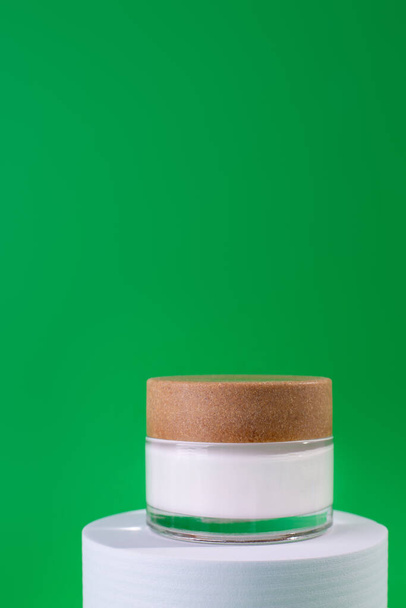 White, glass jar of cream on a stand, white podium on green background.  Design Template of Fashion Cosmetics Product for Ads, flyer, banner or Magazine Background.  - Fotografie, Obrázek