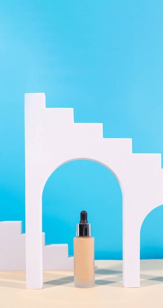 Tekutý podkladový krém s pipetou neznačková láhev na modrém pozadí s obloukem, geometrická postava. BB krém pro profesionální make-up, kapátko pro aplikaci na obličej. Kosmetický ženský doplněk - Fotografie, Obrázek