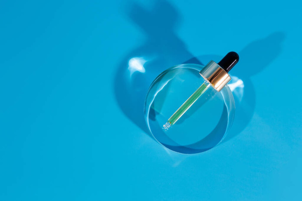 Glaspipette aus Hyaluronsäure auf Glaskreisstütze, blauer Hintergrund. Kosmetikkonzeption - Foto, Bild