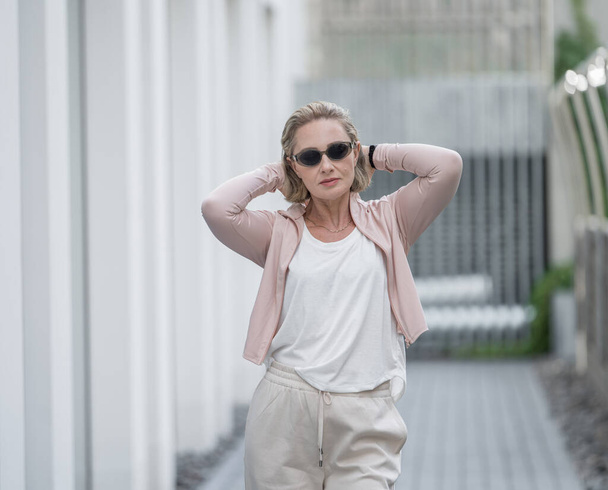 Portret van de mooie witte blanke volwassen vrouw die ze draagt Active Lifestyle Outdoor Sportwear. Donker zonneglas. Vilnius, Litouwen. Wit t-shirt. - Foto, afbeelding