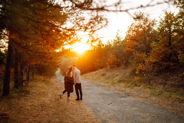 Junges Paar beim Spazierengehen und Kuscheln im Herbstpark bei Sonnenuntergang. Menschen, Lebensstil, Entspannung und Urlaubskonzept. - Foto, Bild