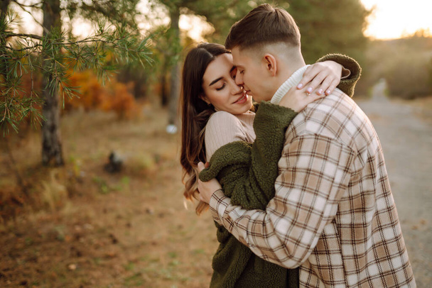 Young couple having fun walking and hugging on autumn park at sunset. People, lifestyle, relaxation and vacations concept. - Фото, изображение