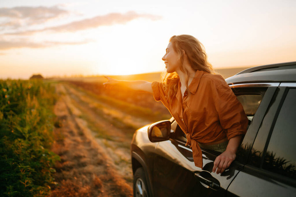 Young woman is resting and enjoying sunset in the car. Lifestyle, travel, tourism, nature, active life. - Foto, imagen