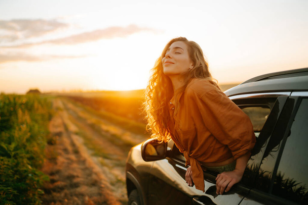 Young woman is resting and enjoying sunset in the car. Lifestyle, travel, tourism, nature, active life. - Foto, Imagem