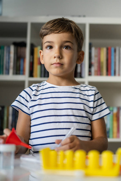 Jeden předškolní chlapec hraje doma sedí u stolu s vědeckými experimenty dívá přímo do kamery s vážným obličejem dětství vyrůstá koncept kopírovat prostor přední pohled - Fotografie, Obrázek