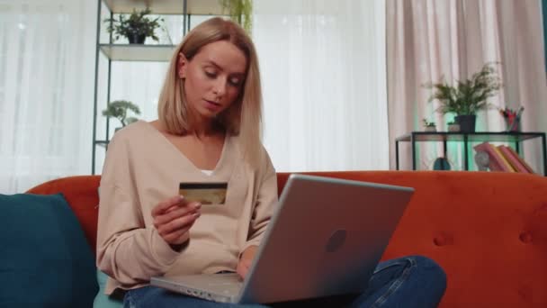 Girl using credit bank card and laptop computer while transferring money, purchases online shopping, order food delivery at home. Young woman sitting on couch holding dollar cash at home living room - Metraje, vídeo