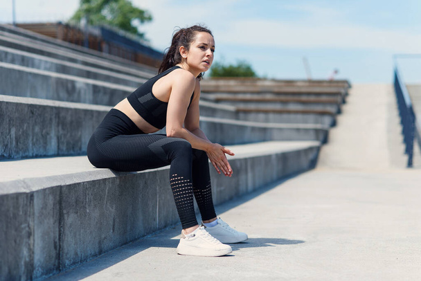 Exhausted pretty woman after hard outdoor training sitting on stairs at sports stadium. Healthy active lifestyle concept. - Foto, Bild