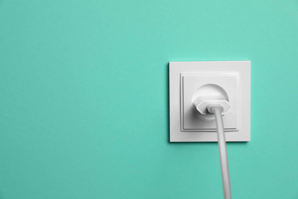 Power socket with inserted plug on turquoise wall, space for text. Electrical supply - Photo, Image