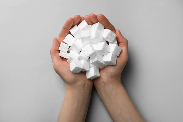 Woman with handful of styrofoam cubes on light grey background, top view - Фото, зображення