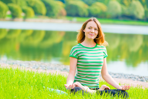 sorrindo menina-yogi executa exercícios em um parque verde perto do la
 - Foto, Imagem