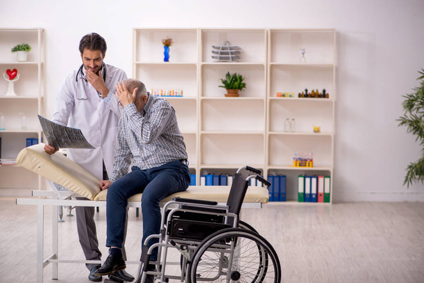 Viejo en silla de ruedas visitando al joven médico radiólogo - Foto, Imagen