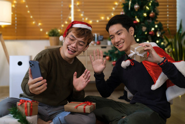 Két boldog férfi ül egy díszített karácsonyfa mellett, és szelfit csinálnak okos telefonnal.. - Fotó, kép