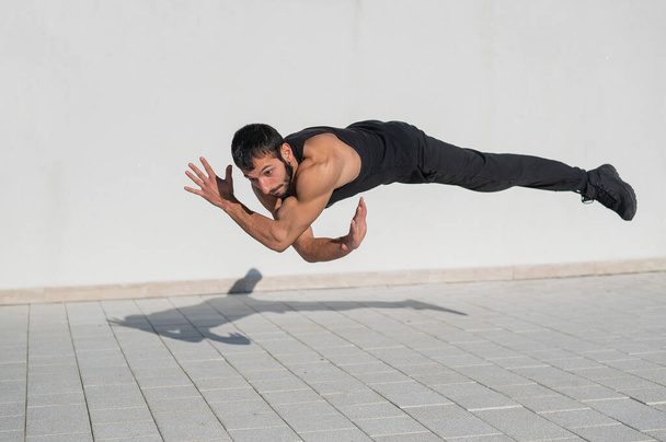 Un homme en tenue de sport noire saute en faisant des pompes à l'extérieur - Photo, image