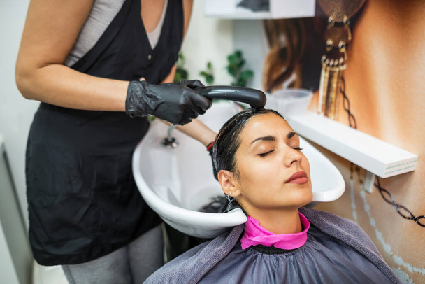 female client washes hair in salon, professional hairdresser washes head of female client with water and shampoo treatment, hairstyle beauty hair care, fashion service. - 写真・画像