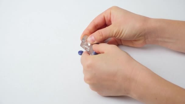 Een vrouw pakt blauwe pillen uit om plaque te detecteren, handen close-up op een witte achtergrond - Video