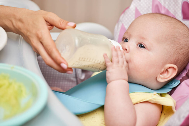 Mom feeds her adorable baby girl from a bottle with milk - Zdjęcie, obraz