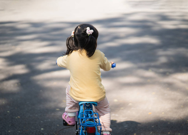 Asyalı kız bebek parkta bisiklet sürmeyi öğreniyor. Çocuk bisiklet pratiği için eğitim konsepti, bebek sporları konsepti. - Fotoğraf, Görsel