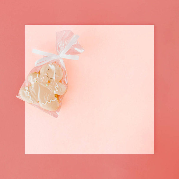 2023. Menselijke vorm peperkoek koekje verpakt in cellofaan tegen pastel koraal-roze achtergrond met licht gekleurde kopieerruimte. Nieuwjaarskaartje idee. Kerstviering concept. Minimale vlakke lay. - Foto, afbeelding