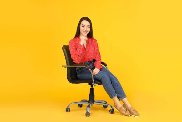Young woman sitting in comfortable office chair on yellow background - Fotoğraf, Görsel