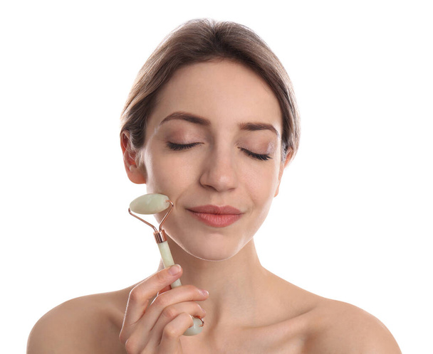 Young woman using natural jade face roller on white background - Fotografie, Obrázek
