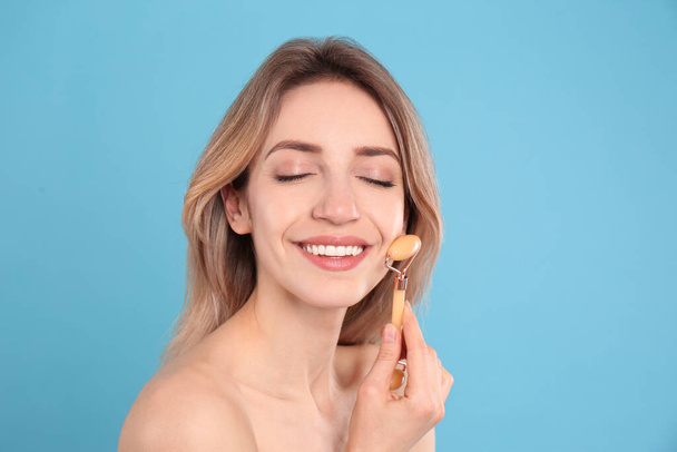 Young woman using natural jade face roller on light blue background - Foto, immagini