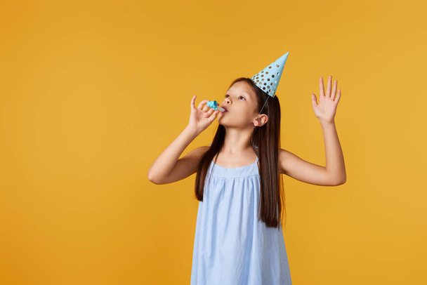 happy little birthday girl with party cone hat and whistle on yellow background. copy space - Photo, Image